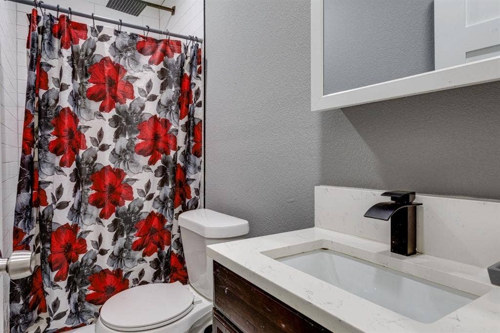 Bathroom featuring a vanity with a white countertop, rectangular basin, and matte black faucet, accented by a shower area with white tile surround and a ceiling-mounted rainfall showerhead