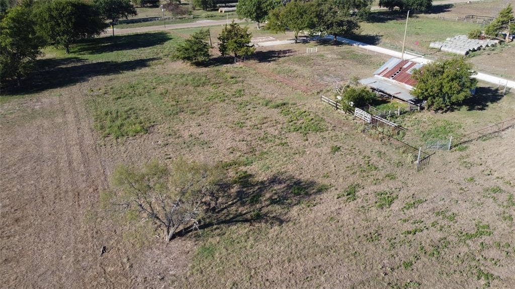 Expansive acreage featuring mature trees, perimeter fencing, and a metal-roofed structure