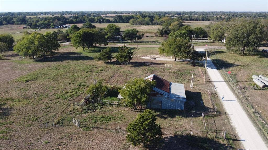 Expansive acreage featuring mature trees, a metal-roof structure, gravel road frontage, and fenced enclosures