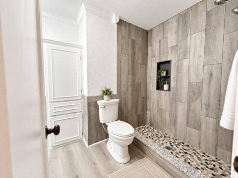 13672 County Road 2915, Eustace, TX 75124 Walk-in shower featuring vertical wood-finish wall tile, a built-in recessed niche, and a stone-tiled floor, complemented by wood-finish flooring and paneled cabinetry