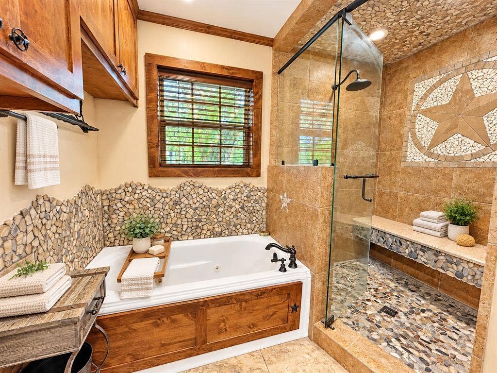 13672 County Road 2915, Eustace, TX 75124 Soaking tub with custom wood paneling and stone tile surround, walk-in shower featuring pebble tile flooring, built-in stone bench, glass enclosure, and oil-rubbed bronze hardware