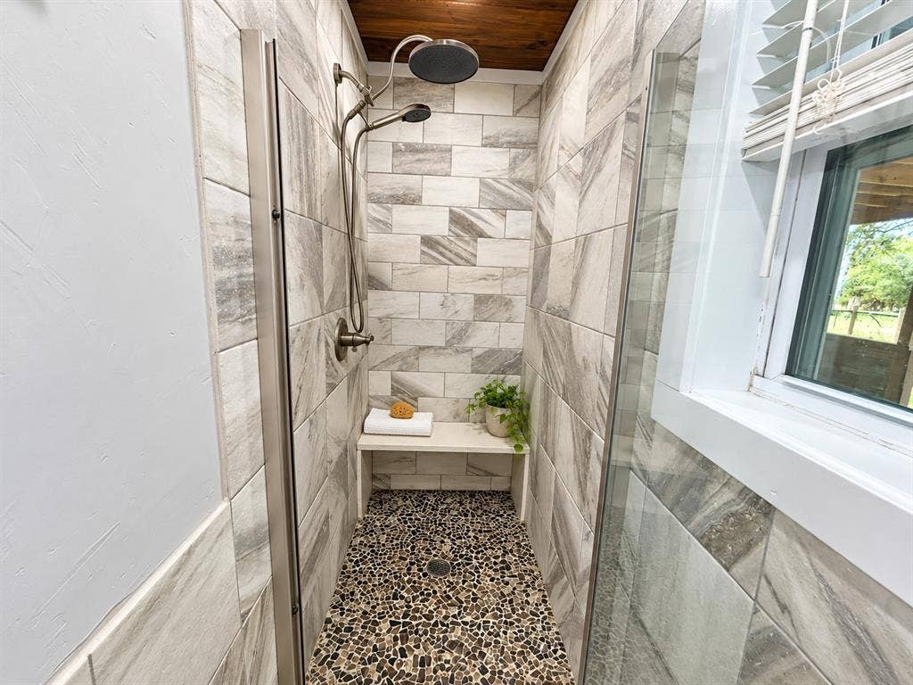 13672 County Road 2915, Eustace, TX 75124 Walk-in shower featuring large-format neutral tile wall cladding, a built-in bench seat, a pebble-stone shower floor, a wood-plank ceiling, and a metallic dual-head shower fixture with glass surround