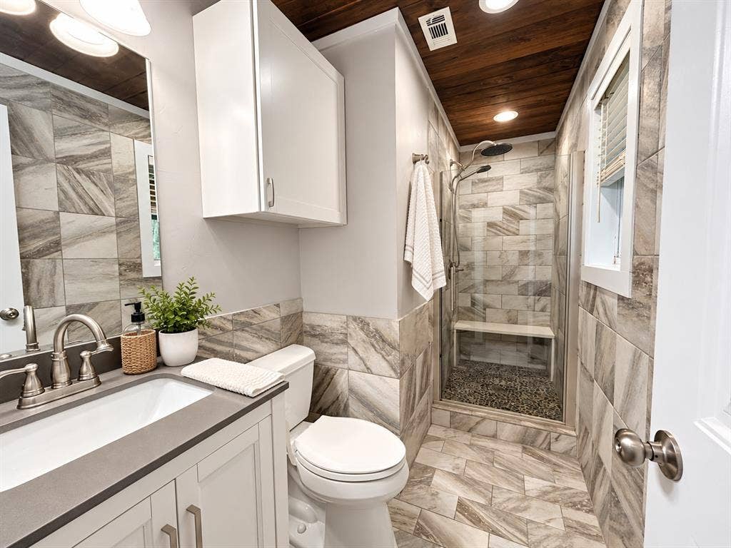 13672 County Road 2915, Eustace, TX 75124 Bathroom featuring large-format decorative wall and floor tile, wood-plank ceiling, glass-enclosed shower with a built-in bench, and a solid-surface vanity countertop with an undermount sink