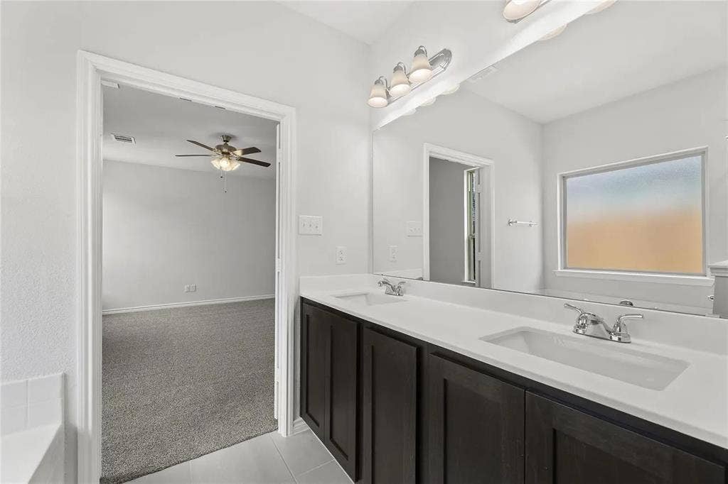 Double-sink vanity with dark cabinetry, solid-surface countertop, chrome fixtures, and a large-format vanity mirror with integrated lighting
