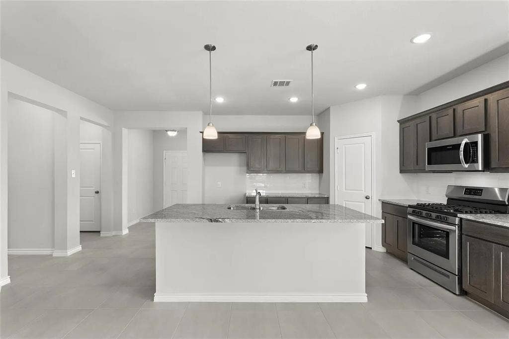 Kitchen featuring a center island with stone-finish countertops, dark wood cabinetry, stainless steel appliances, and dual pendant lighting