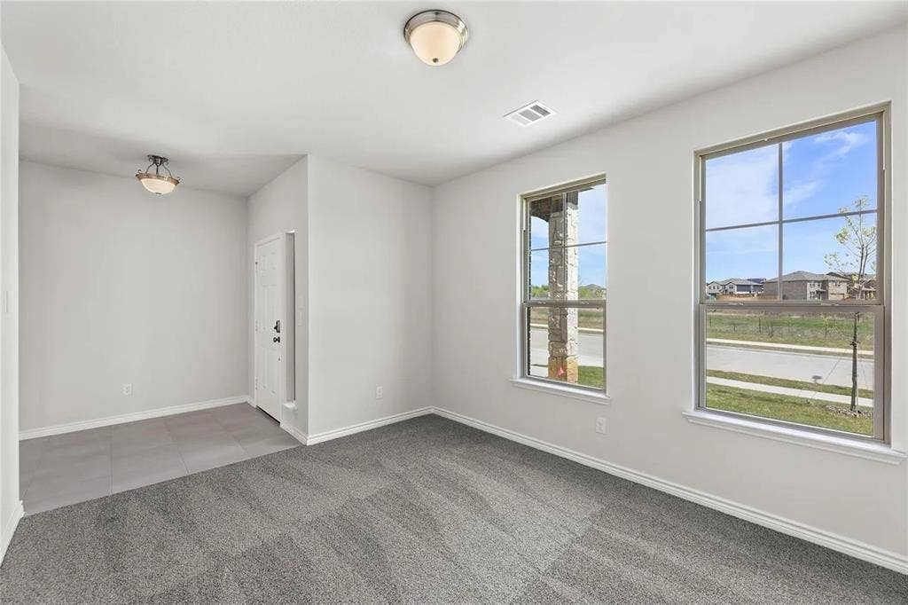 Interior space featuring neutral wall paint, carpeted flooring, large grid-pattern windows, and two flush-mount light fixtures