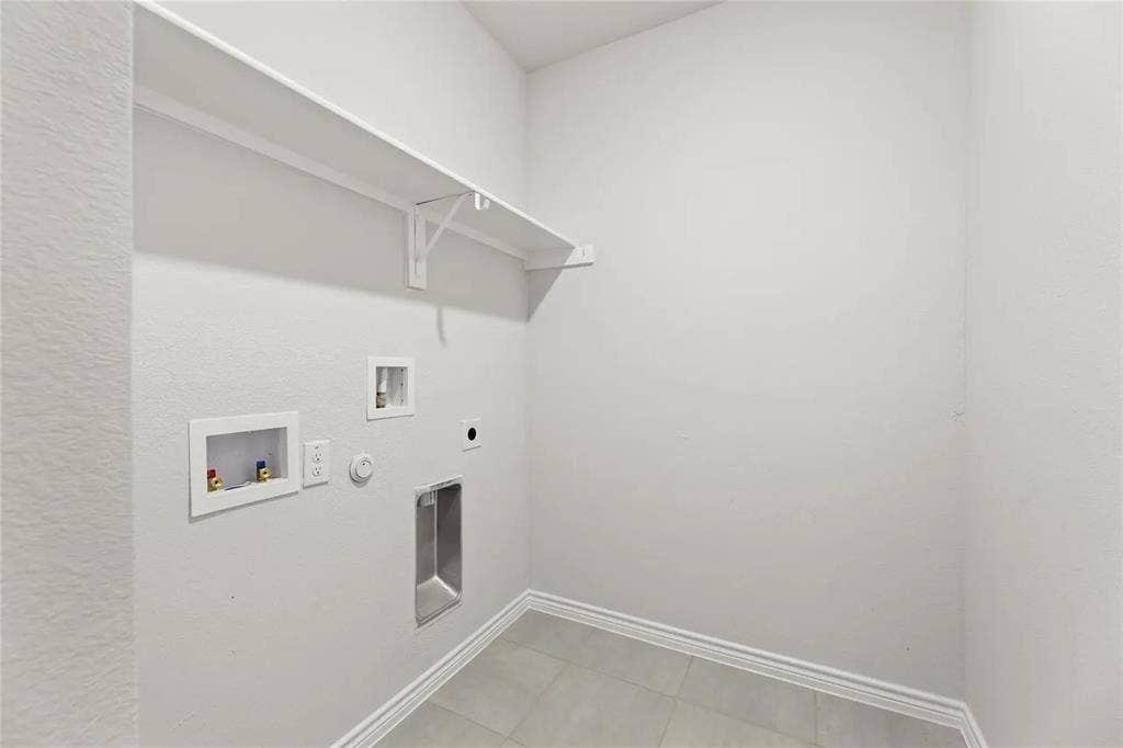 Utility area featuring neutral tile flooring, white wall-mounted shelving, and recessed plumbing connections