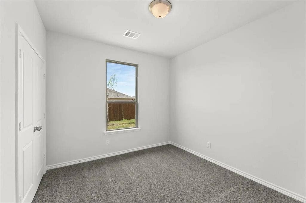 Neutral-toned interior space featuring neutral wall paint, wall-to-wall carpeting, a single-panel interior door, and a flush-mount ceiling light fixture