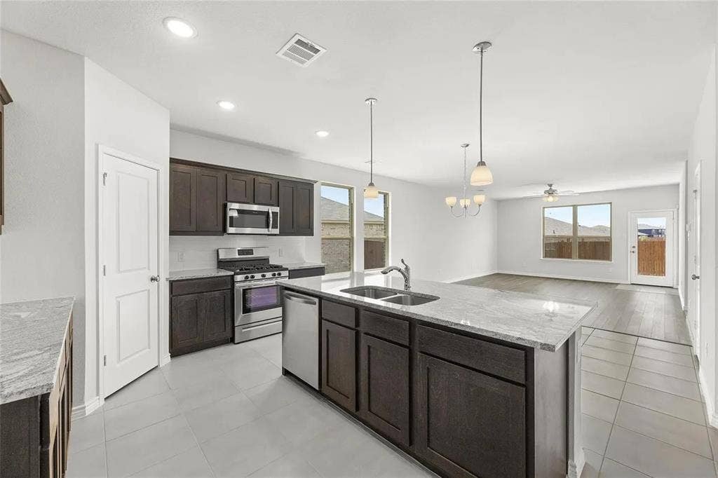 Kitchen featuring dark cabinetry, stone-surface countertops, stainless steel appliances, a central island with an integrated sink, and tile flooring