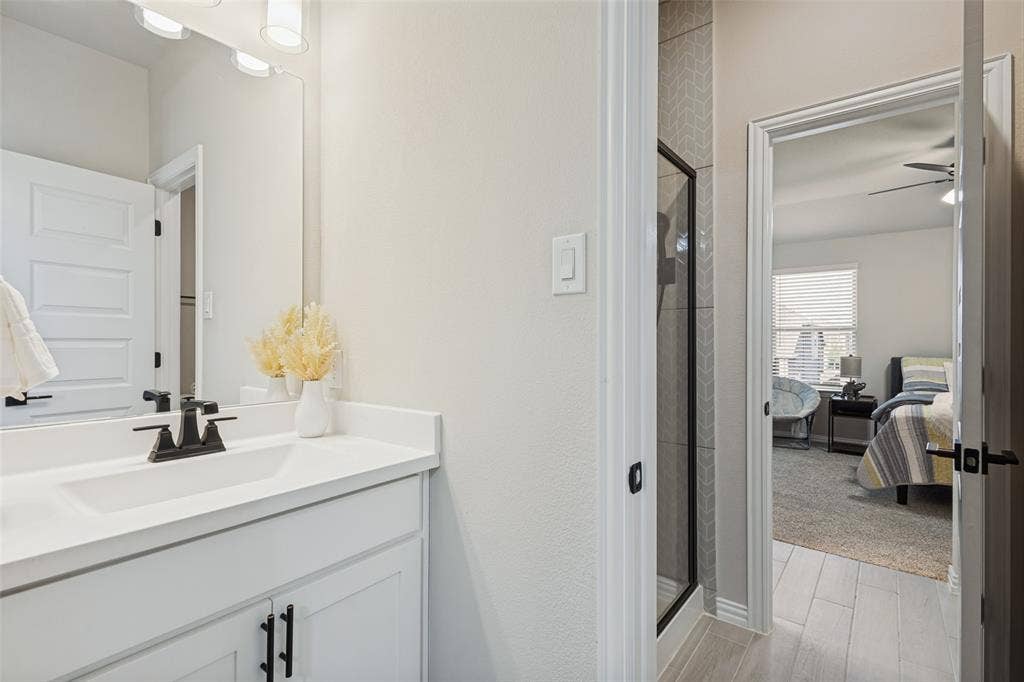 5313 Pratt Circle, McKinney, TX 75071 Bathroom vanity with solid surface countertop, rectangular under-mount sink, and matte black hardware, accompanied by a shower featuring herringbone-patterned tile and a glass enclosure