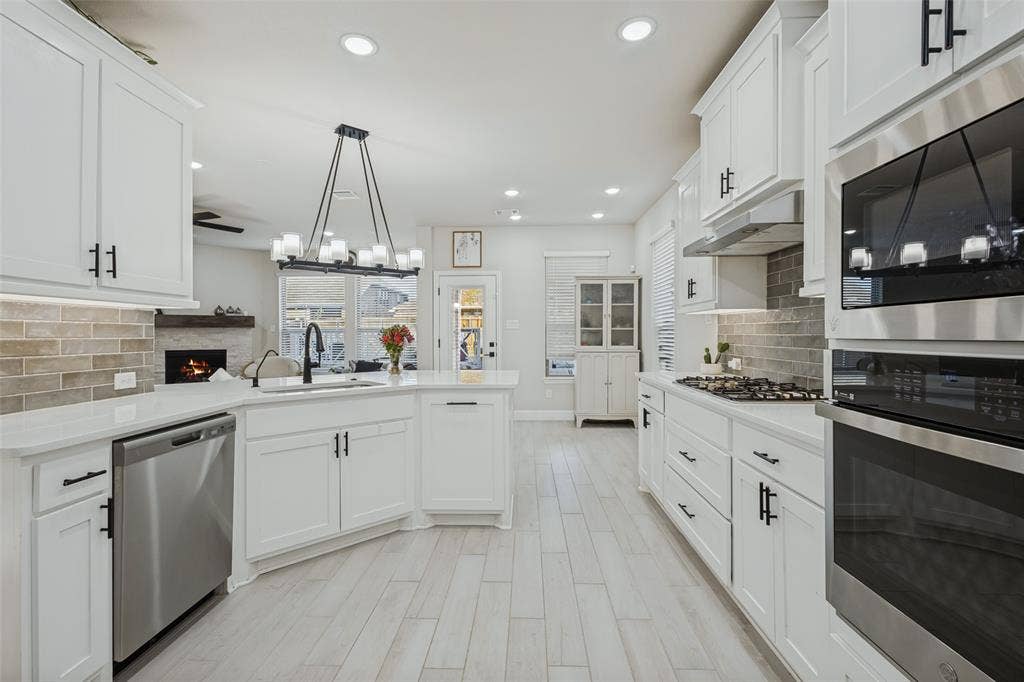 5313 Pratt Circle, McKinney, TX 75071 Kitchen featuring white shaker-style cabinetry, stainless steel appliances, a multi-light linear pendant fixture, subway tile backsplash, and light-toned wood-finish flooring