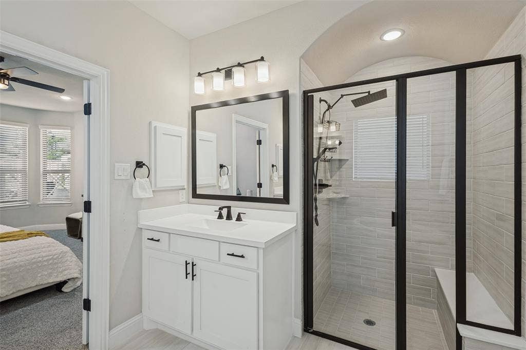 5313 Pratt Circle, McKinney, TX 75071 Bathroom featuring a vanity with a rectangular sink, black-finish hardware, a framed mirror, a four-light fixture, and a tiled shower stall with a built-in bench and glass enclosure