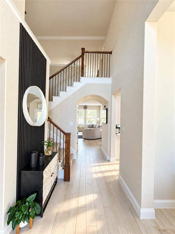 5313 Pratt Circle, McKinney, TX 75071 Foyer featuring vertical slat wall detailing, wood-finish flooring, and a staircase with a wooden handrail and metal balusters under a decorative archway