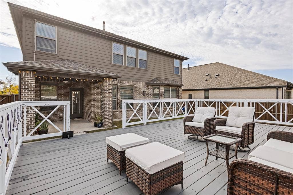 5313 Pratt Circle, McKinney, TX 75071 Expansive elevated deck featuring composite wood-finish decking and white cross-buck railing, complemented by a covered patio with brick pillars and horizontal siding exterior