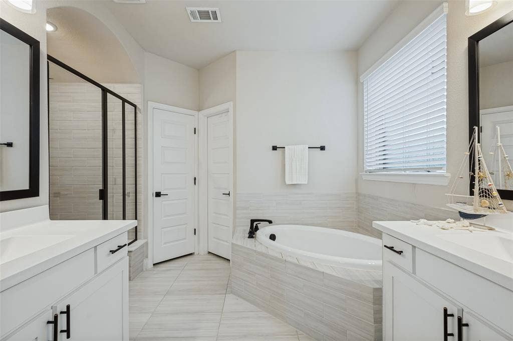 5313 Pratt Circle, McKinney, TX 75071 Bathroom featuring dual white vanities with solid-surface countertops, soaking tub with tile surround, glass-enclosed walk-in shower, and large-format tile flooring