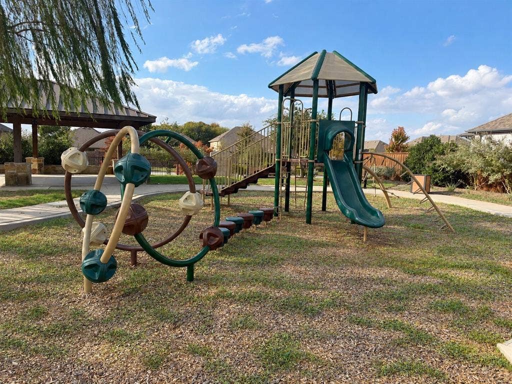 5313 Pratt Circle, McKinney, TX 75071 Outdoor recreation area featuring a multi-level playground structure with a slide and climbing equipment, situated on a mulched surface with an attached pavilion