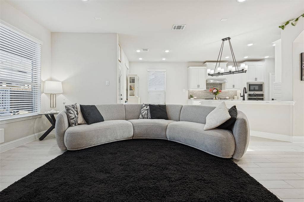 5313 Pratt Circle, McKinney, TX 75071 Open-concept living space featuring wood-finish tile flooring, recessed lighting, white shaker-style cabinetry, a stone-tiled backsplash, and a multi-light linear chandelier