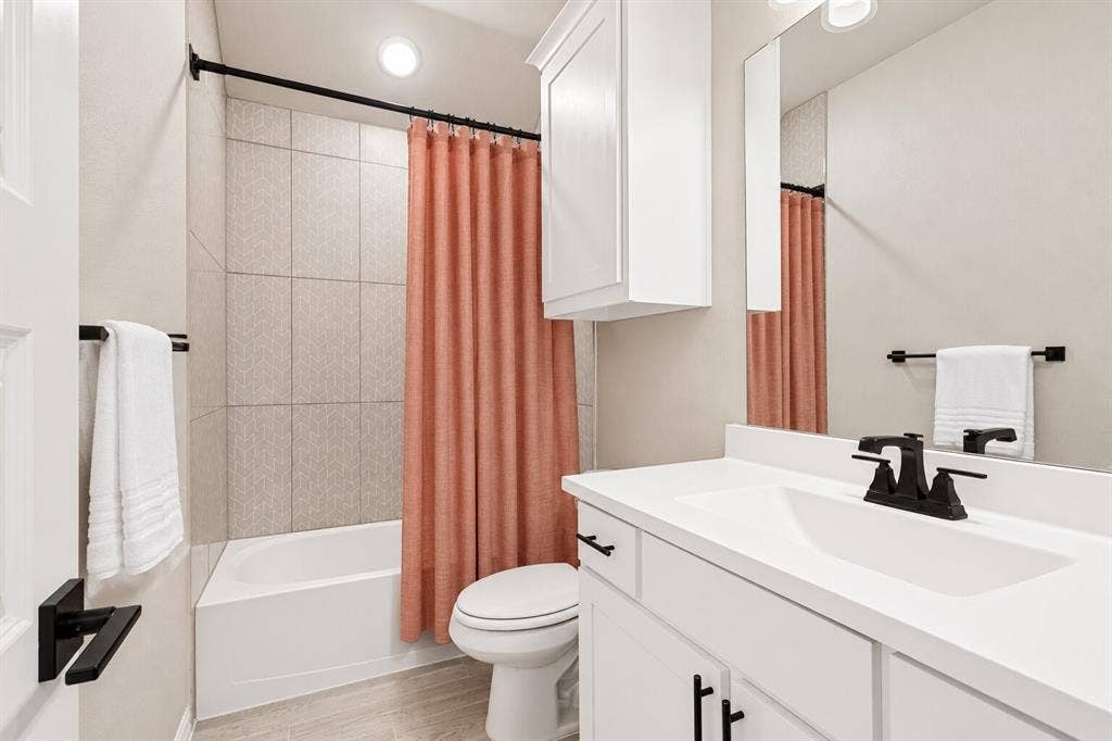 5313 Pratt Circle, McKinney, TX 75071 Bathroom featuring a white vanity cabinet, solid-surface countertop with integrated sink, matte black hardware, wall-mounted medicine cabinet, and a tiled tub-shower surround
