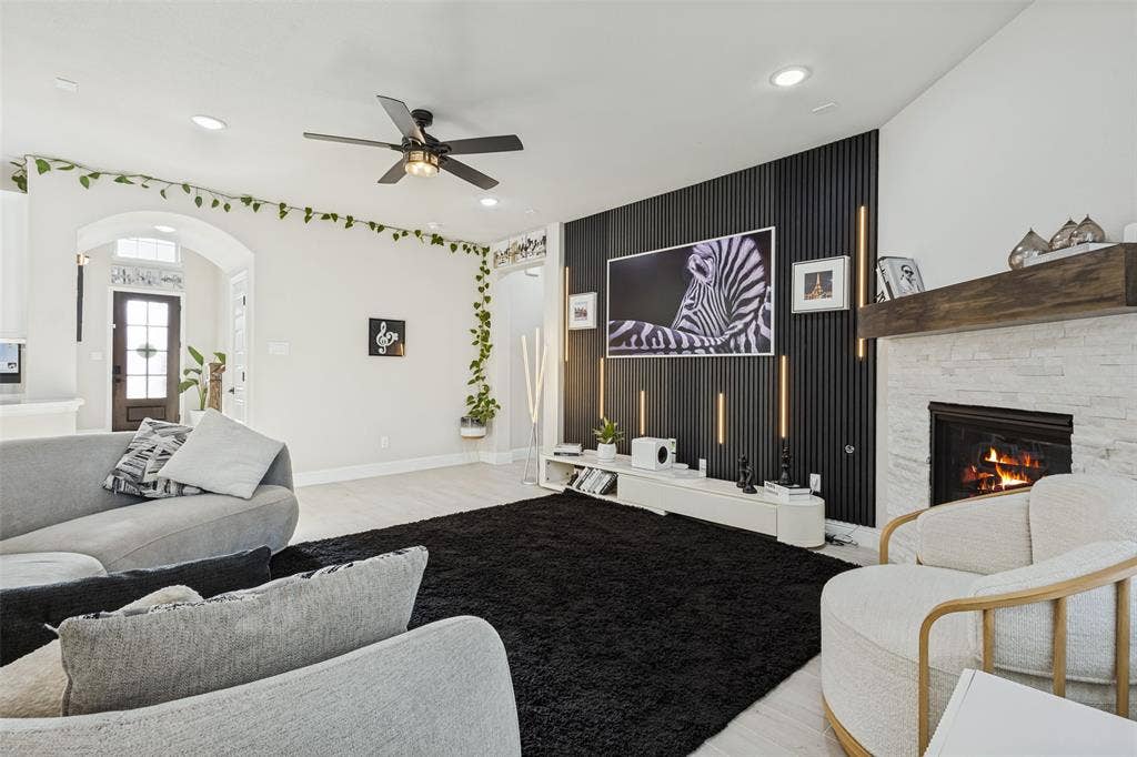 5313 Pratt Circle, McKinney, TX 75071 Living area featuring a vertical slat accent wall with integrated lighting, a stone-surround fireplace with a timber mantel, recessed ceiling lights, and a ceiling fan
