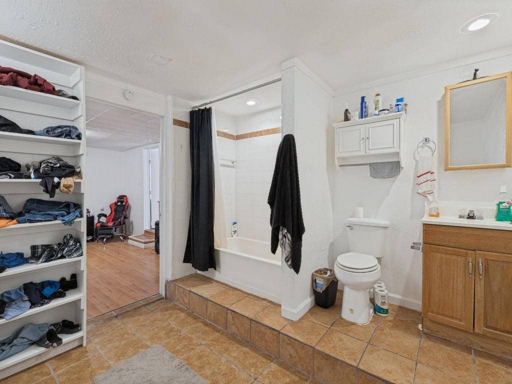 2009 Pecan Street, Commerce, TX 75428 Bathroom featuring ceramic tile flooring, a raised tub surround, a wood-finish vanity with a built-in medicine cabinet, and integrated shelving