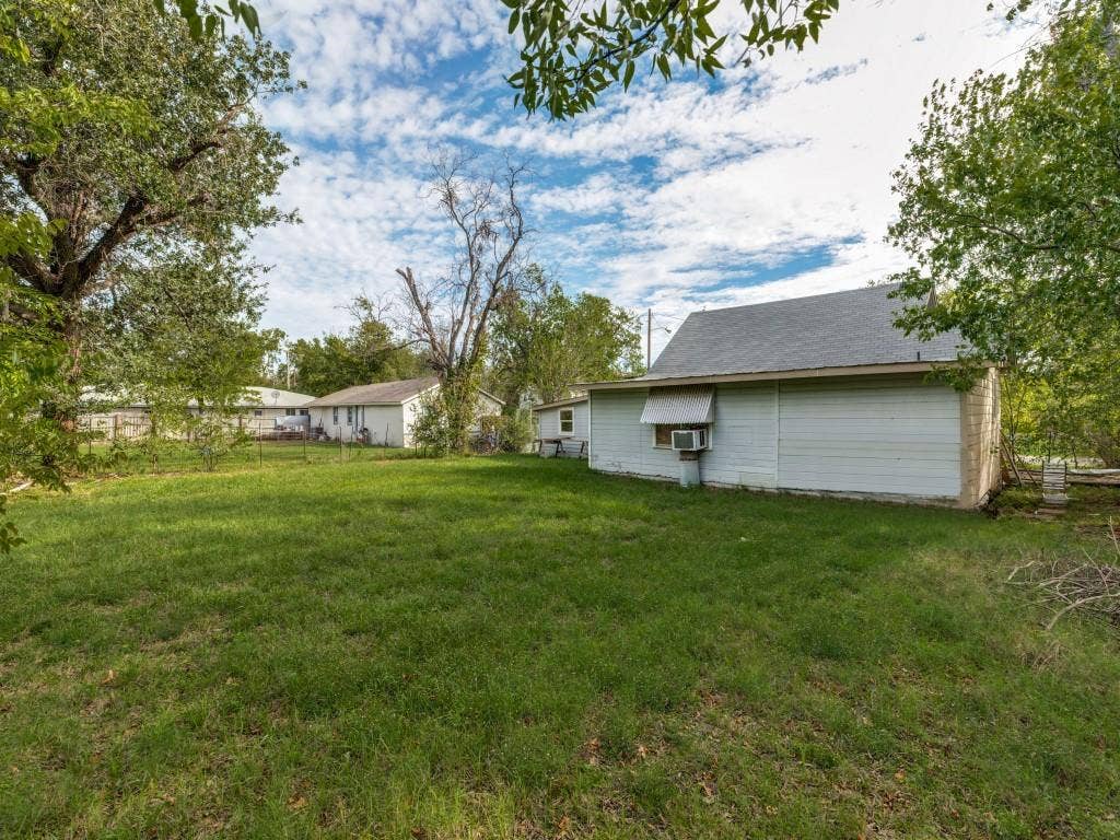 2009 Pecan Street, Commerce, TX 75428 Expansive backyard featuring a large grass lawn, mature trees, and a detached outbuilding with a metal awning