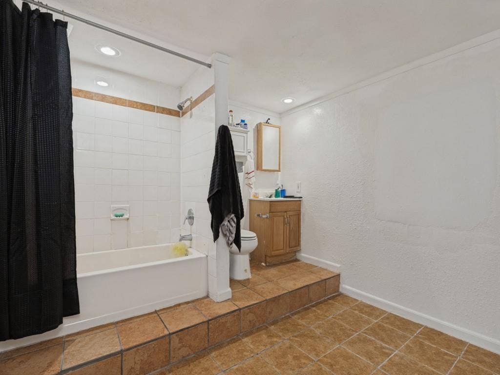 2009 Pecan Street, Commerce, TX 75428 Bathroom featuring a raised platform floor with ceramic tile, a shower-tub combination with white wall tile, a wooden vanity cabinet, and recessed ceiling lighting