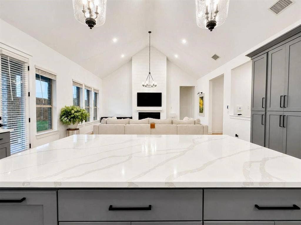 8912 Free Ferry Lane, McKinney, TX 75071 Expansive kitchen island with a white quartz countertop, floor-to-ceiling gray cabinetry, vaulted ceilings, and a fireplace with shiplap detailing