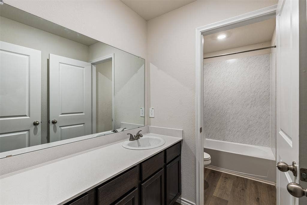 Bathroom vanity featuring dark-toned cabinetry, a light-colored solid surface countertop, an integrated sink with a dual-handle faucet, and a wall-to-wall mirror