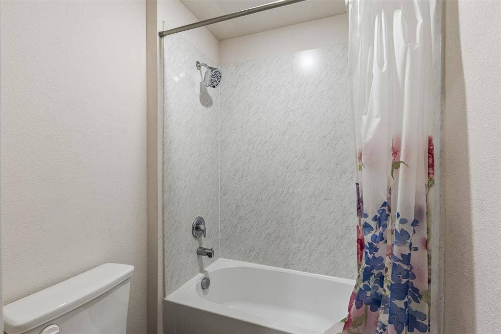 Full-size bathtub with light-toned wall surround, shower head, chrome-finish plumbing fixtures, and a dual-flush toilet