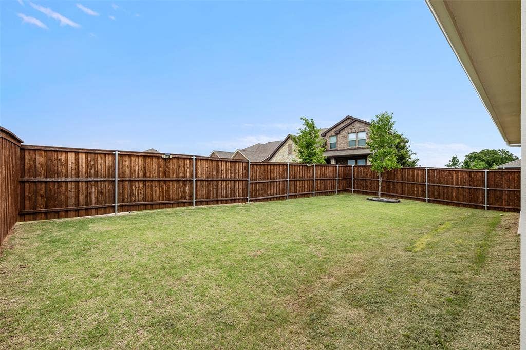 Fenced backyard featuring a manicured lawn, wood-finish privacy fencing, and a mature tree