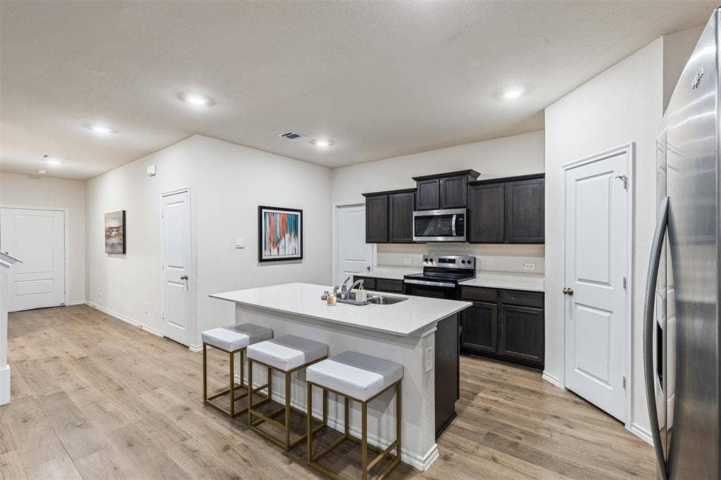 Kitchen featuring wood-finish flooring, a central island with a solid-surface countertop, dark-toned cabinetry, recessed lighting, and stainless steel appliances