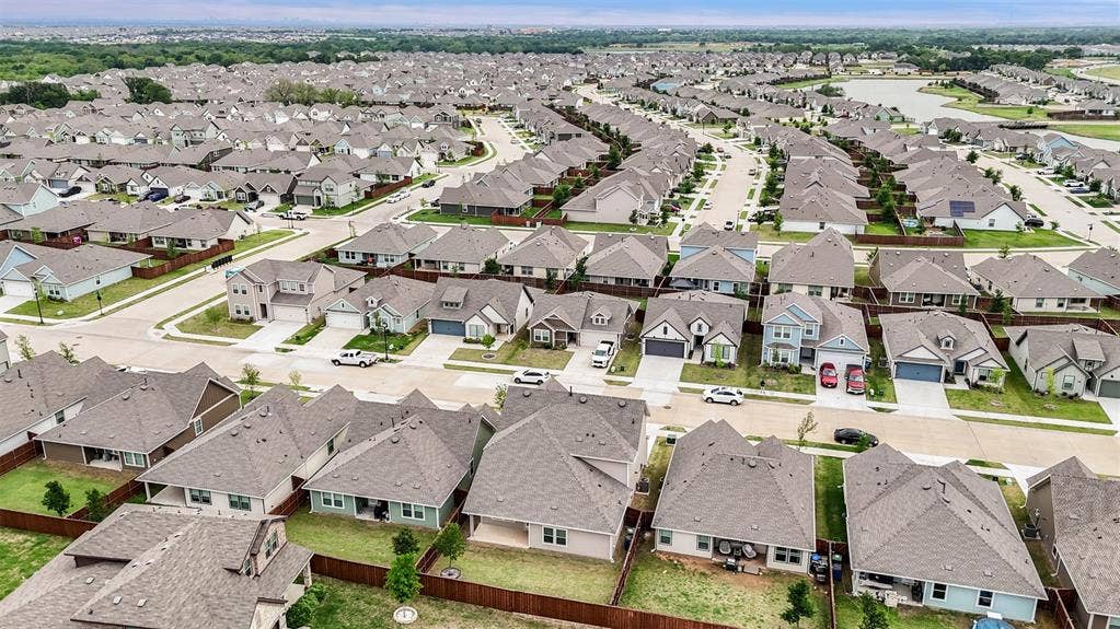 Aerial perspective of a master-planned community featuring residential lots with fenced backyards, paved streets, and a retention pond