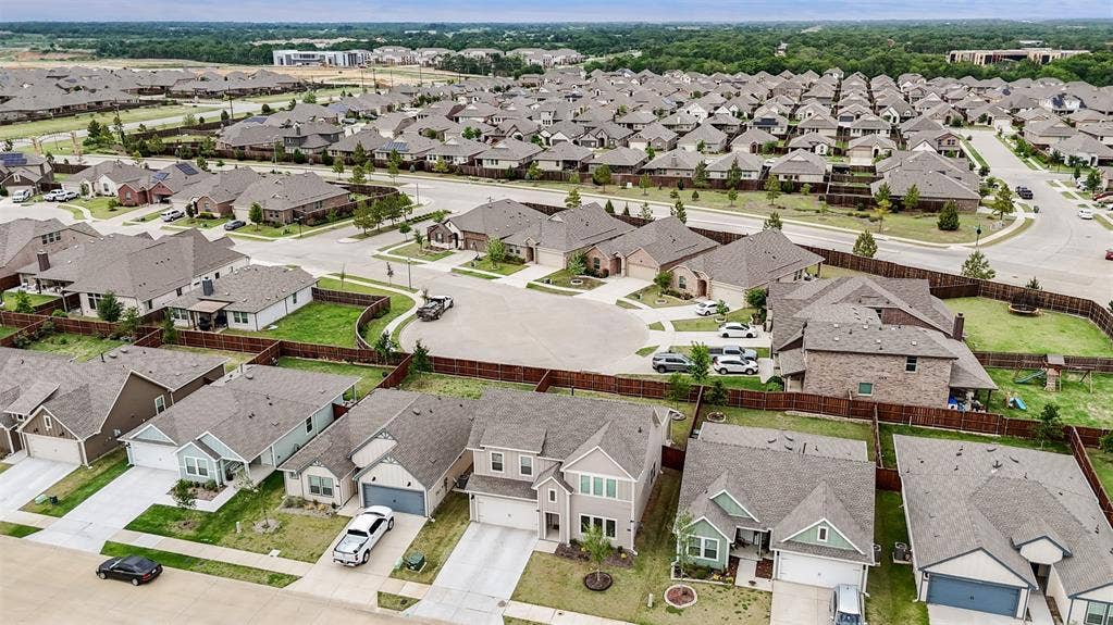Aerial perspective of a suburban neighborhood featuring residential homes, paved streets, concrete driveways, and private fenced backyards
