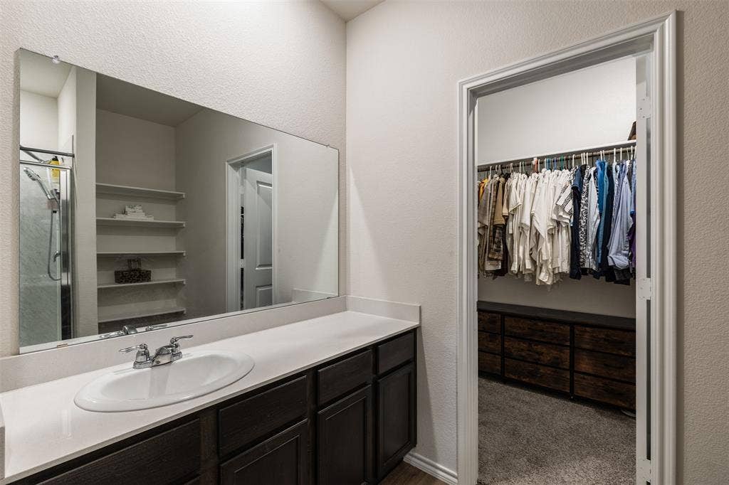 Bathroom featuring a dark-finish wood vanity with a solid-surface countertop, integrated oval basin, large wall-mounted mirror, and a walk-in closet equipped with built-in shelving and drawer storage