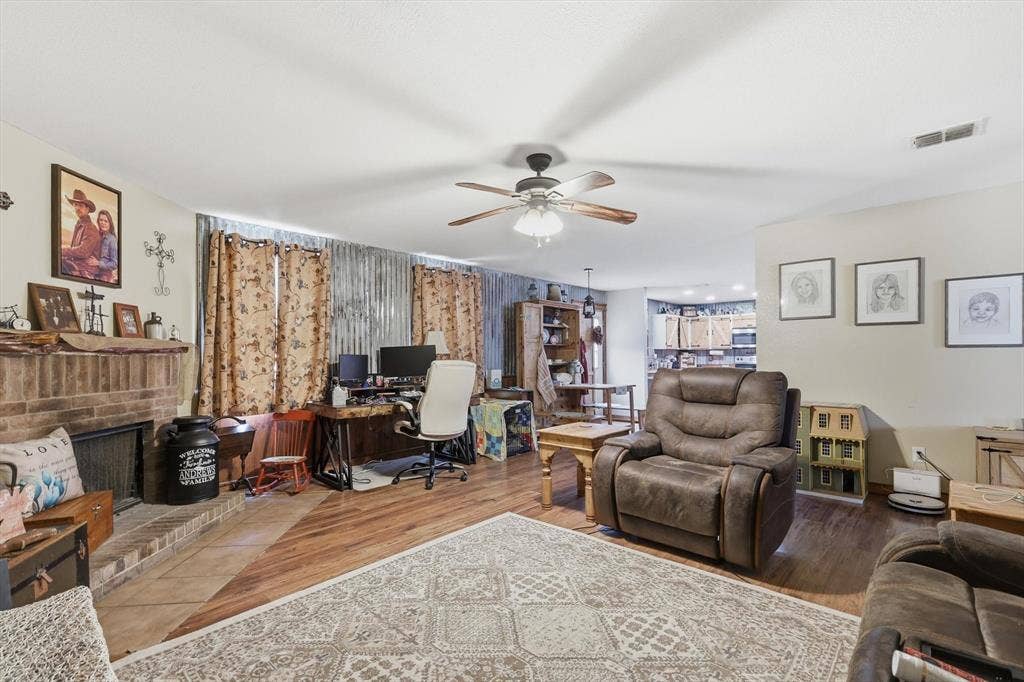 1633 Sierra Meadow Lane, Fort Worth, TX 76247 Brick fireplace with a rustic mantel, wood-finish flooring, metal accent wall, and a ceiling-mounted light fixture with a fan