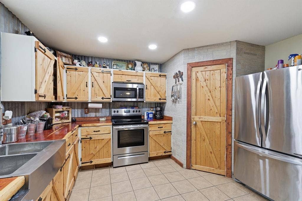 1633 Sierra Meadow Lane, Fort Worth, TX 76247 Kitchen featuring custom wood cabinetry with barn-door detailing, stainless steel appliances, corrugated metal backsplash, tiled flooring, and a metal apron-front sink