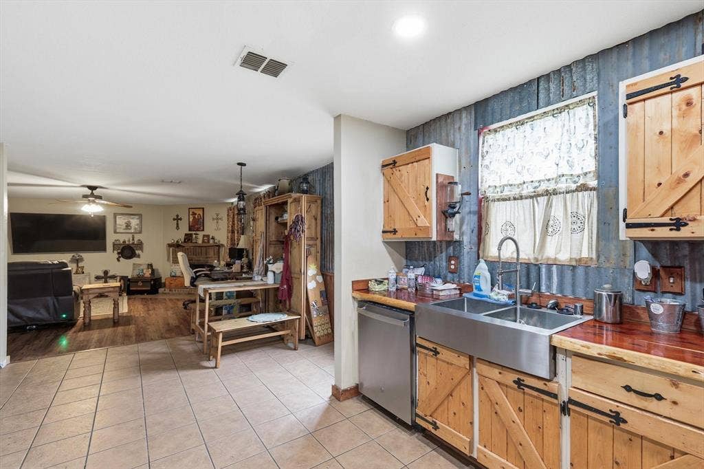1633 Sierra Meadow Lane, Fort Worth, TX 76247 Kitchen featuring custom wood cabinetry with sliding barn-style doors, corrugated metal wall accents, a stainless steel apron-front sink, and polished wood-finish countertops