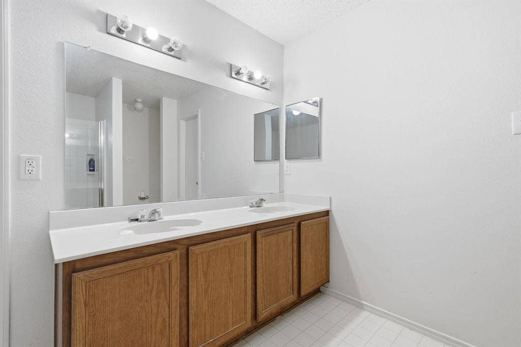 1633 Sierra Meadow Lane, Fort Worth, TX 76247 Double vanity featuring wood-finish cabinetry, a solid-surface countertop with integrated dual sinks, a large wall-mounted mirror, and multi-bulb polished chrome light fixtures
