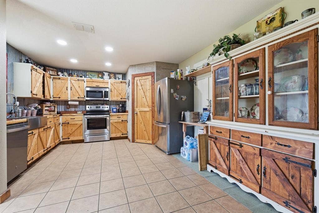 1633 Sierra Meadow Lane, Fort Worth, TX 76247 Kitchen featuring custom wood cabinetry with sliding barn-style door detailing, stainless steel appliances, farmhouse sink, recessed lighting, and tile flooring