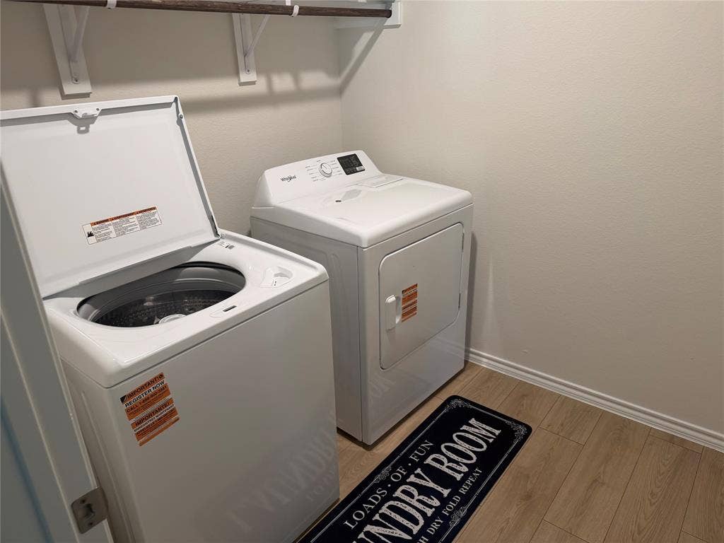 Laundry area featuring a top-load washer, front-load dryer, and wall-mounted shelving unit over wood-finish flooring