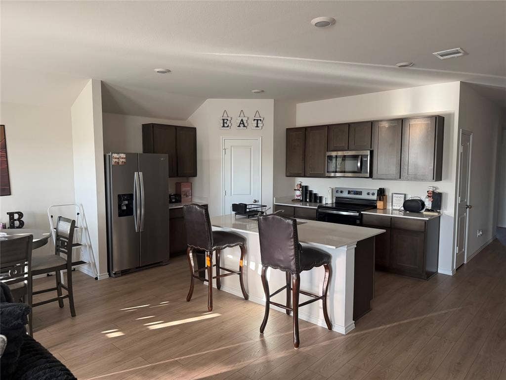 Kitchen featuring dark-finish cabinetry, stone-surface countertops, center island with seating, stainless steel appliances, and wood-finish flooring