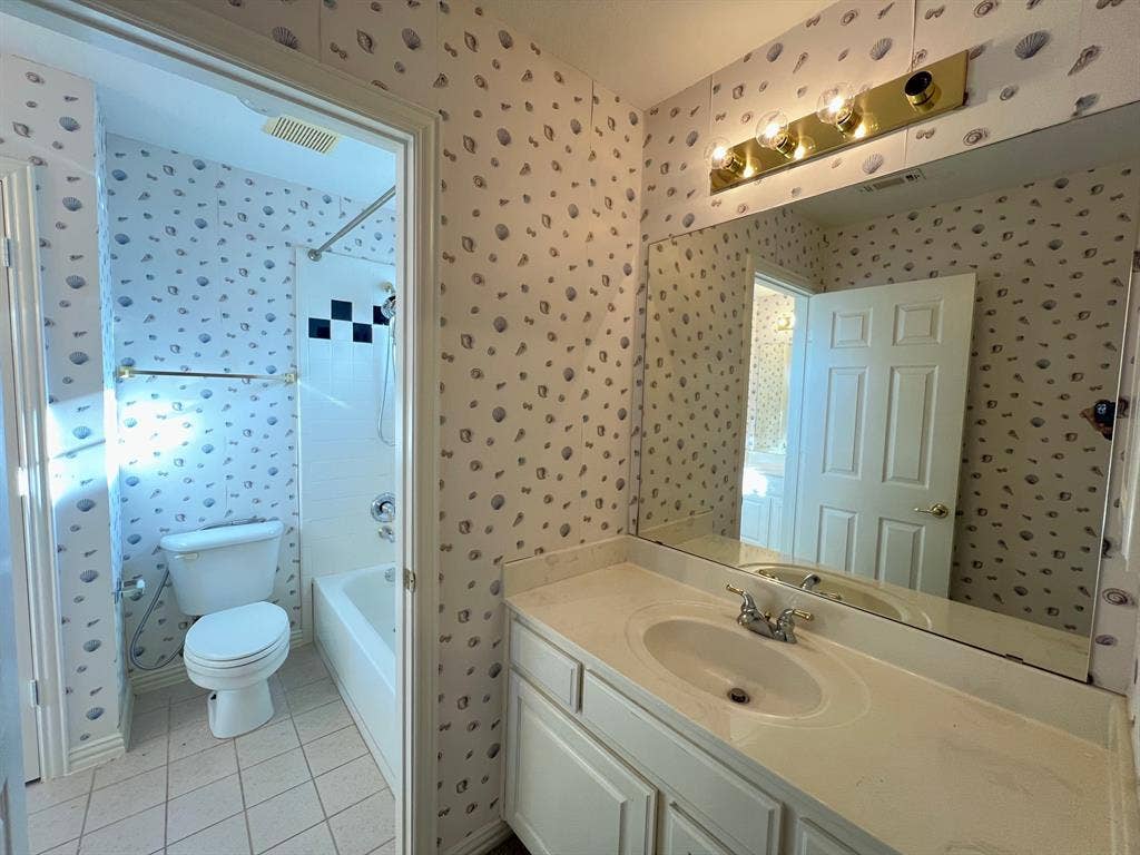 Single-basin vanity with a solid-surface countertop, large wall-mounted mirror, brass-finish light fixture, and tiled flooring
