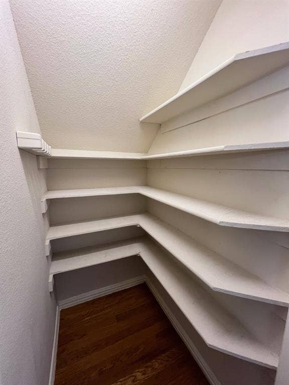 Storage area featuring four levels of built-in shelving and wood-finish flooring