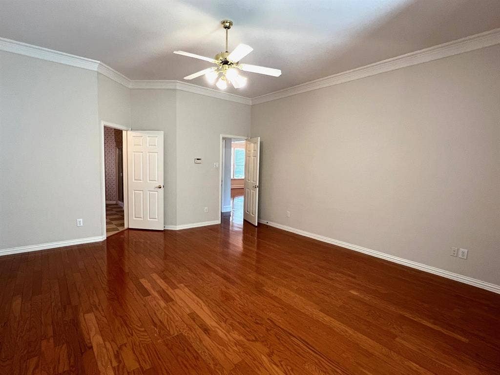 Room interior featuring wood-finish flooring, vaulted ceilings with crown molding, and a central ceiling fan with multi-light fixture