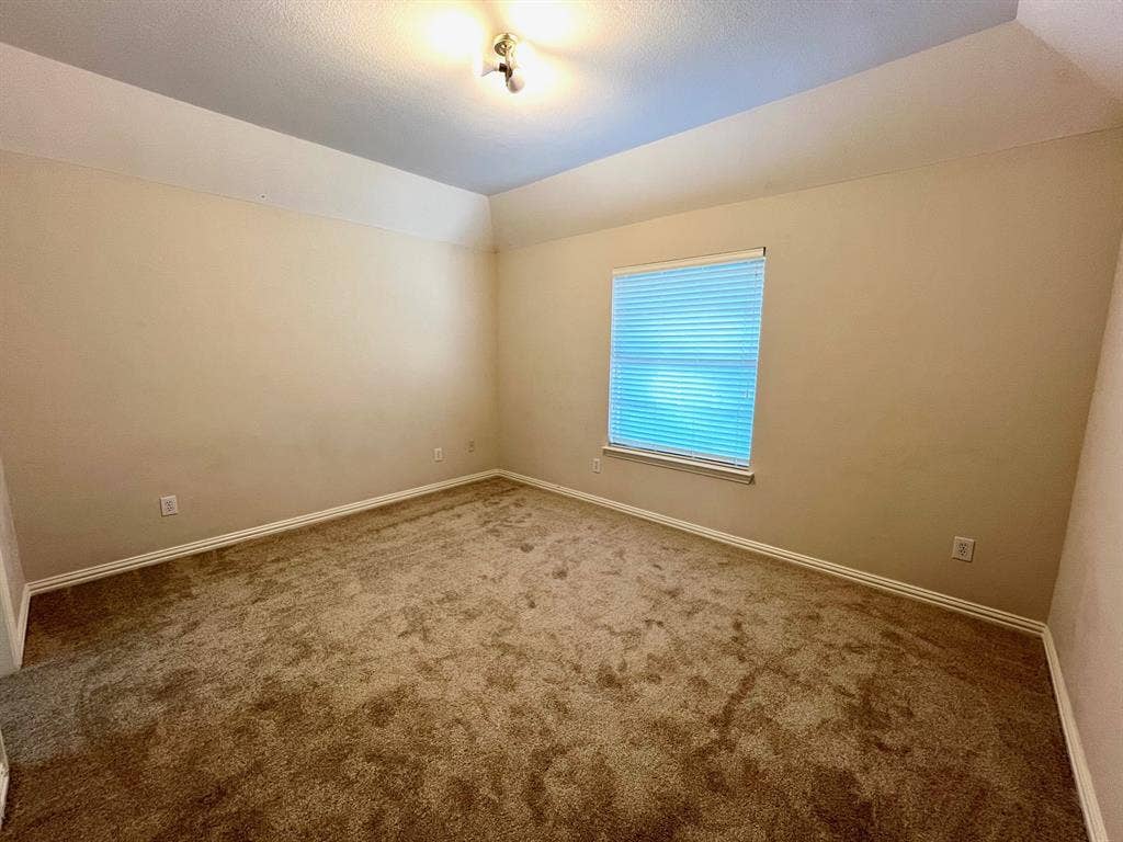 Room featuring neutral wall tones, plush wall-to-wall carpeting, vaulted ceilings, and a single window with installed blinds