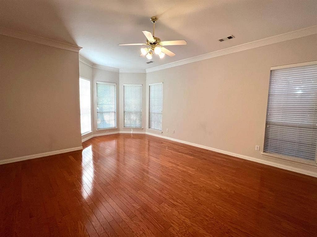 Spacious room featuring wood-finish flooring, crown molding, a bay window configuration, and a central ceiling fan with integrated lighting
