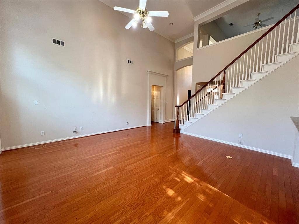 Two-story living area featuring vaulted ceilings, wood-finish flooring, a staircase with a wooden handrail, a mezzanine overlook, and a ceiling fan
