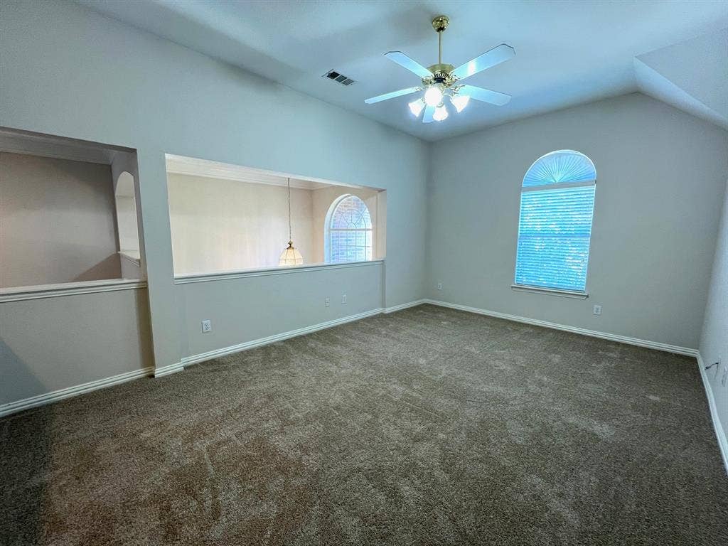 Vaulted ceilings, arched window, wall cut-out, ceiling fan, and carpeted flooring