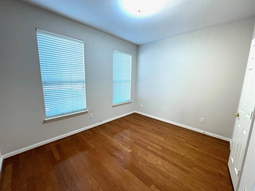 Room featuring wood-finish flooring, neutral wall paint, two windows with horizontal blinds, and a paneled interior door