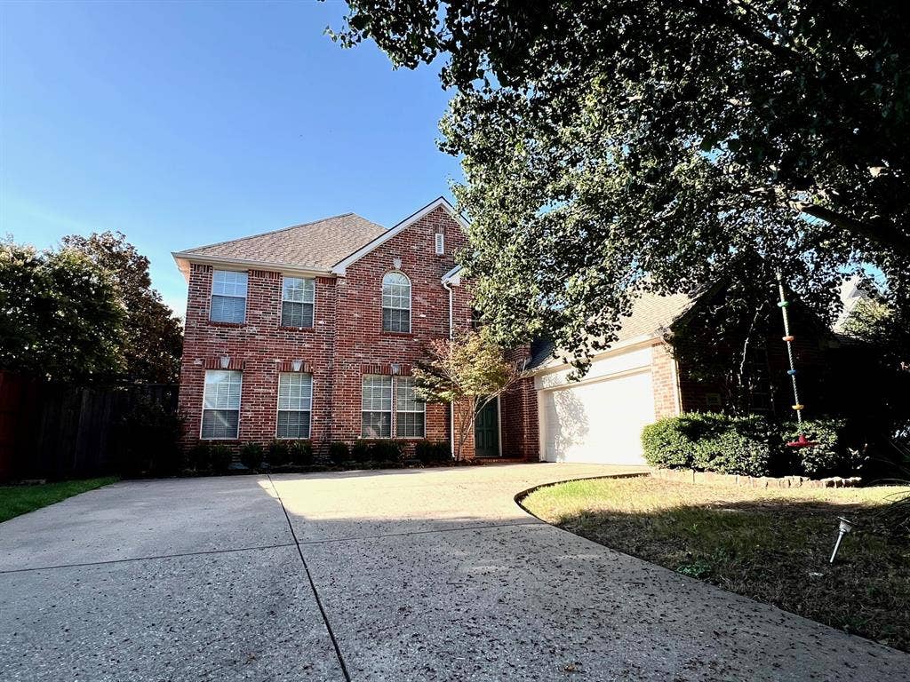 Two-story brick exterior featuring a multi-gabled roofline, arched window detailing, and an attached two-car garage with a concrete driveway